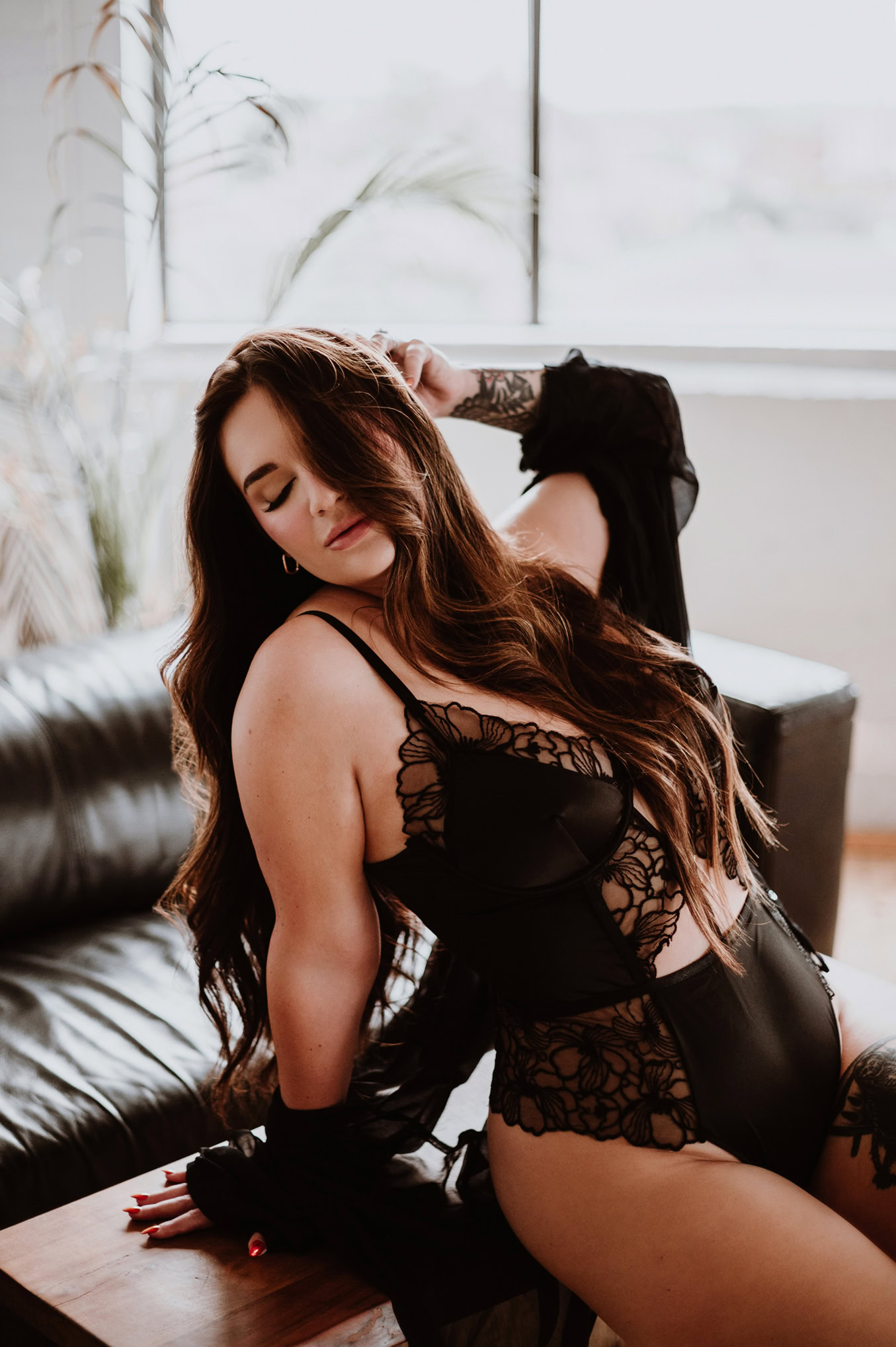 Woman posing confidently in a black lace bodysuit during a boudoir photo shoot
