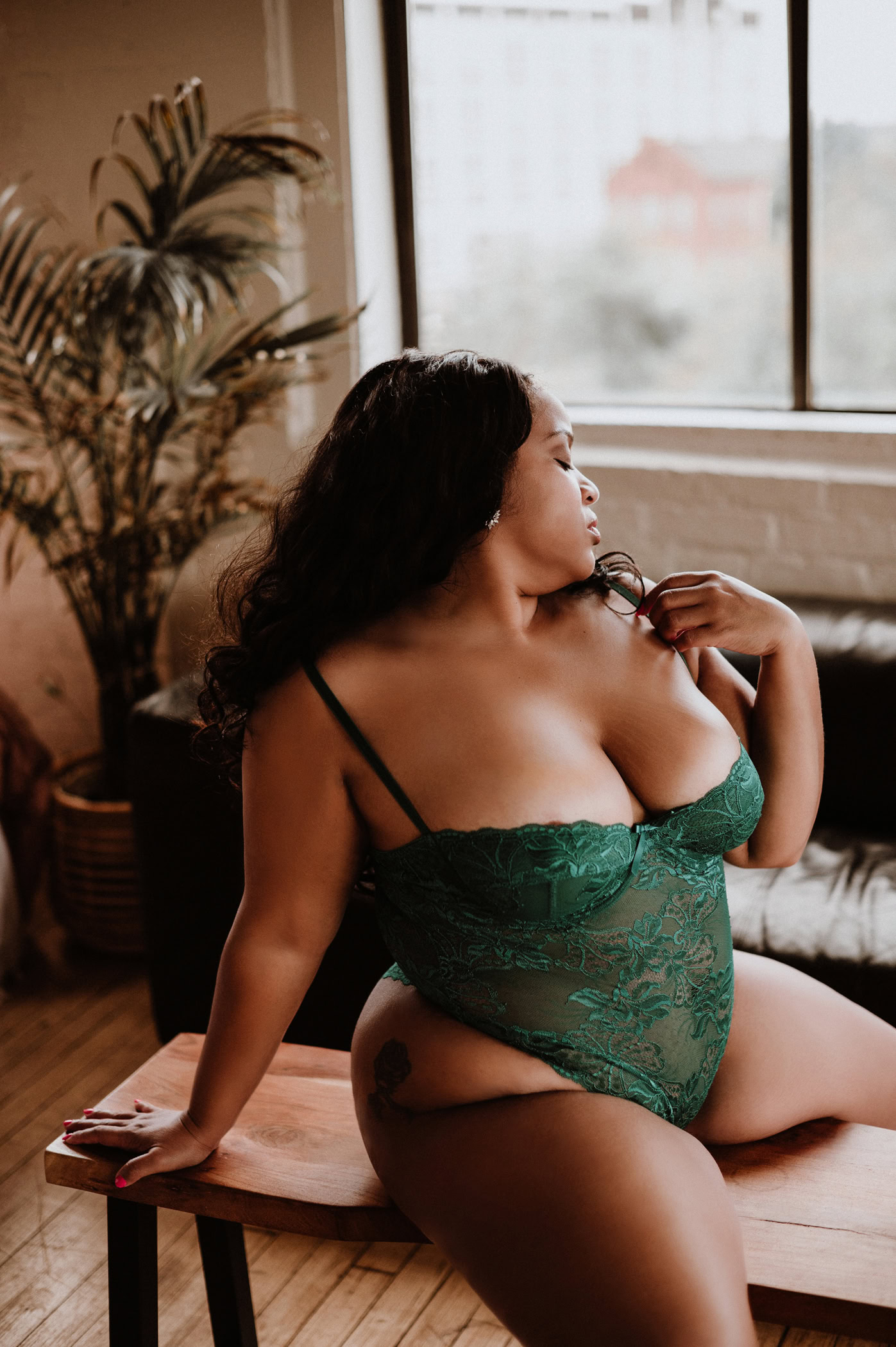 Woman in green lace bodysuit sitting confidently on a wooden bench during a boudoir session