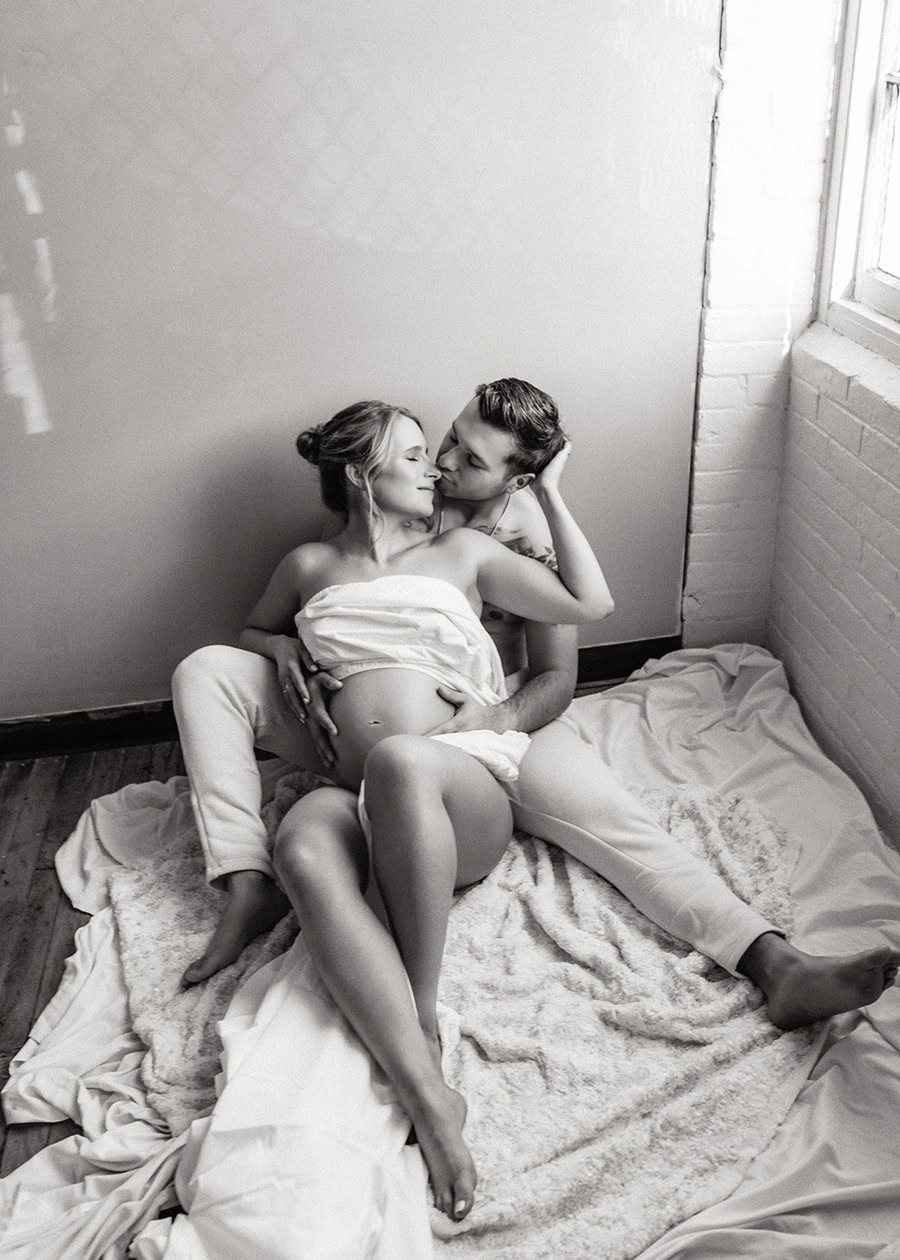 Couple embracing in white sheets during a maternity boudoir session in Connecticut.