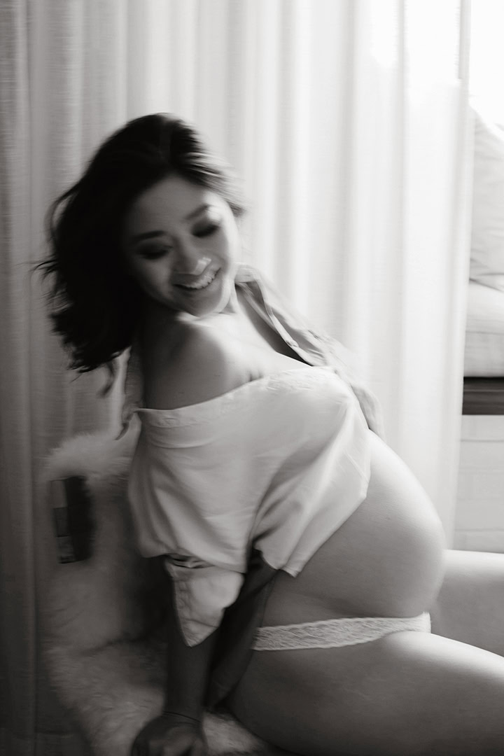 Expecting mother moving through pose, blurry in natural light during a maternity boudoir session in Connecticut.