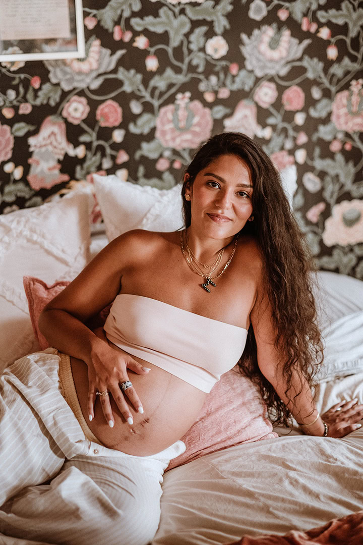 Pregnant woman posing on a bed during a cozy maternity boudoir session in Connecticut.