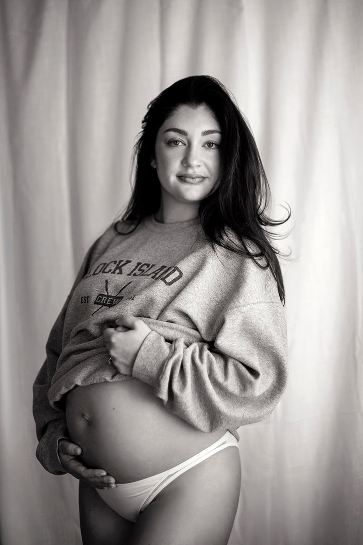 Pregnant woman wearing a casual sweatshirt during a relaxed maternity boudoir photography session.