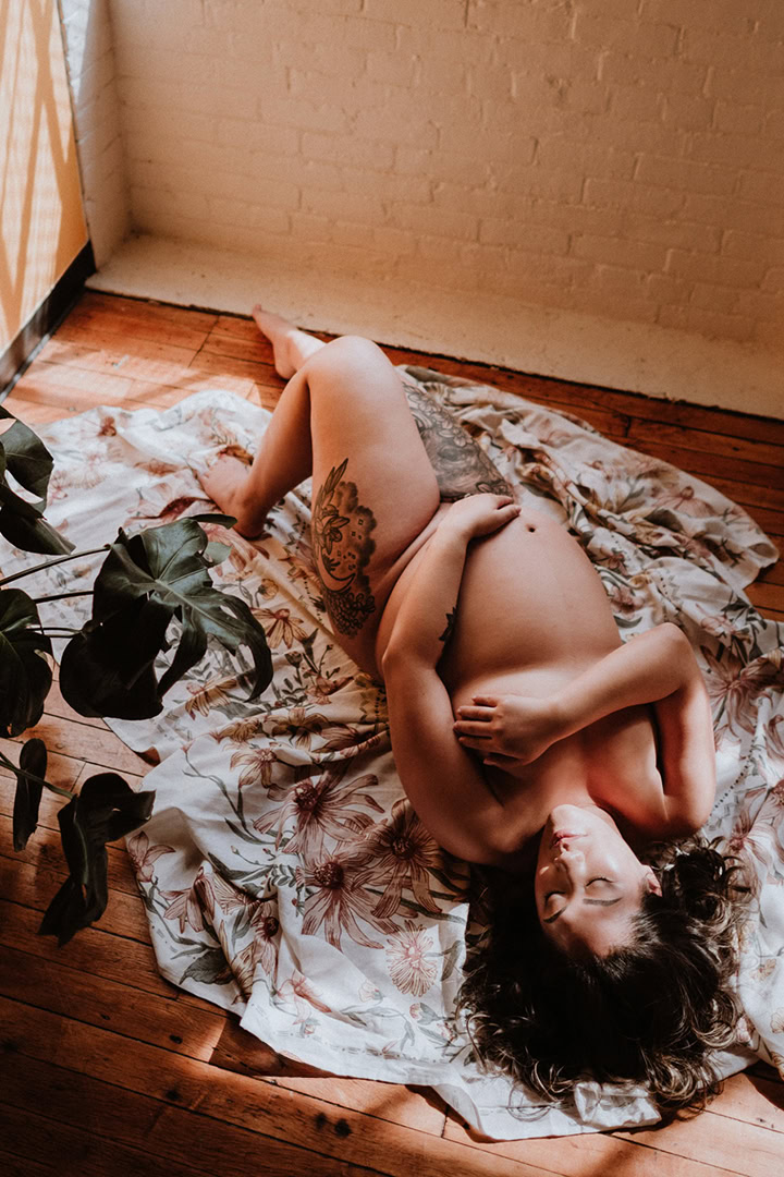 Expecting mother reclining on floral fabric during an artistic maternity boudoir photography session in Connecticut.